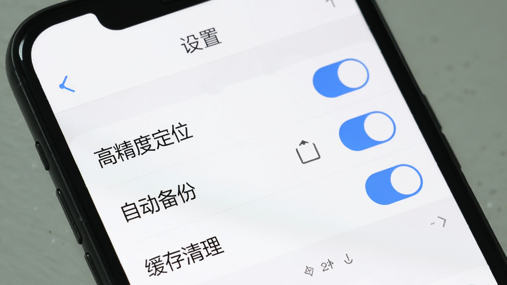 手机屏幕上显示易拍水印打卡相机的设置页面,页面中有“高精度定位”、“自动备份”、“缓存清理”等选项开关,开关为蓝色开启状态,背景为白色,整体界面简洁清晰,有“设置”标题栏。画质干净,排版整齐,无多余元素。