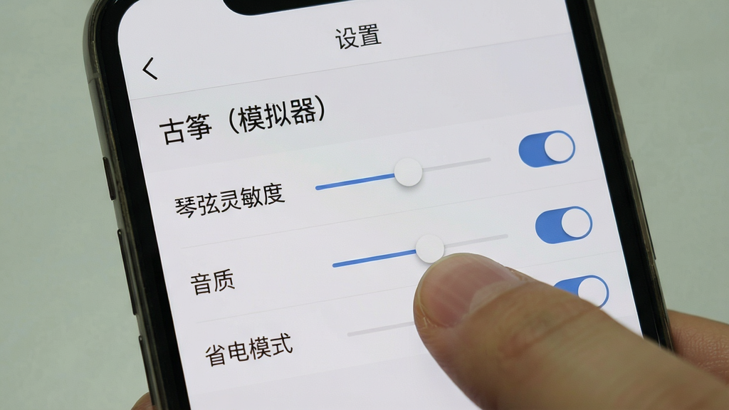 主体:手机屏幕上显示“古筝(模拟器)”的设置界面,展示“琴弦灵敏度”、“音质”、“省电模式”等选项。布局:界面为列表式,每个选项右侧有滑动条或开关。排版:清晰规整,背景为浅灰色,文字为深灰色。风格:简洁实用,符合工具类应用的设计风格。细节:一个手指正在拖动灵敏度滑动条,屏幕顶部有“设置”字样。画质:干净,无多余元素。