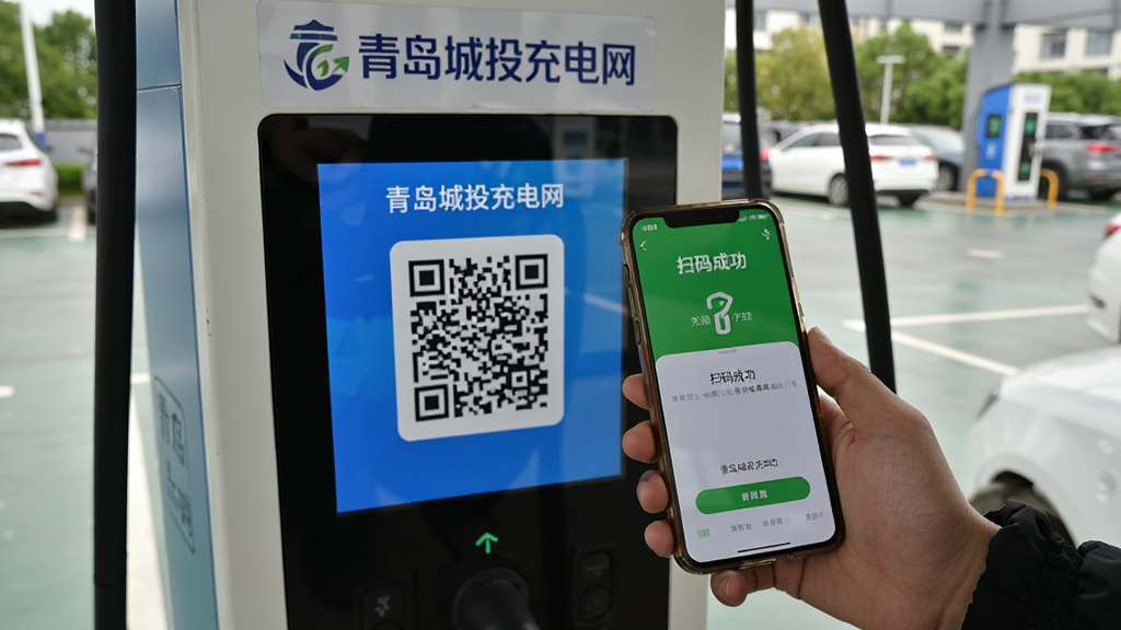 主体:用户手持手机扫描充电桩上的二维码,充电桩屏幕显示“青岛城投充电网”。布局:手机和充电桩在画面中央,背景为停车场。排版:二维码放大显示,手机屏幕显示充电启动成功。风格:纪实摄影风格,自然真实。细节:充电桩上贴有“青岛城投充电网”标识,手机界面显示“扫码成功”。画质:清晰,噪点少,无多余元素。